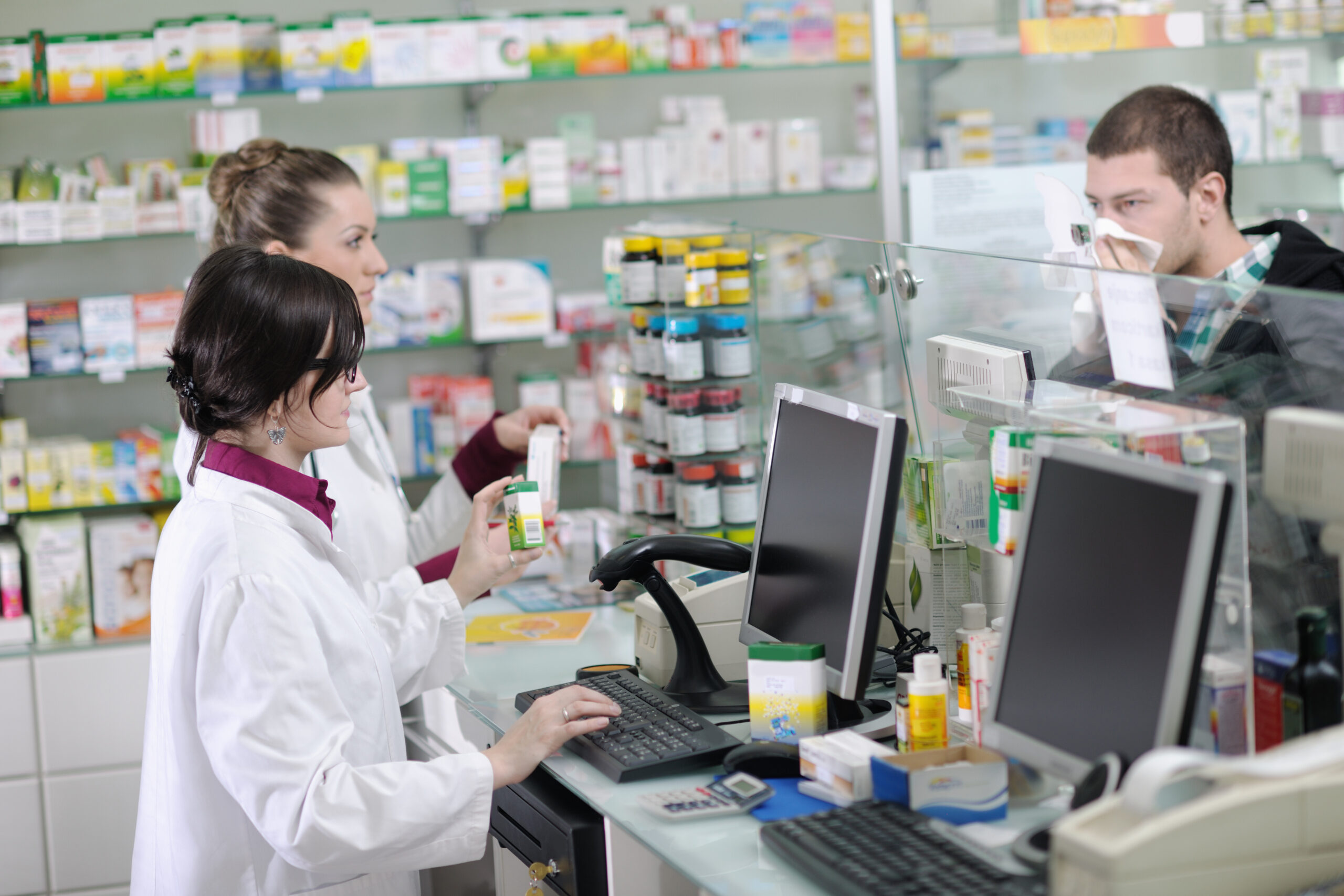 a foto mostra duas farmacêuticas atendendo um rapaz gripado numa farmácia