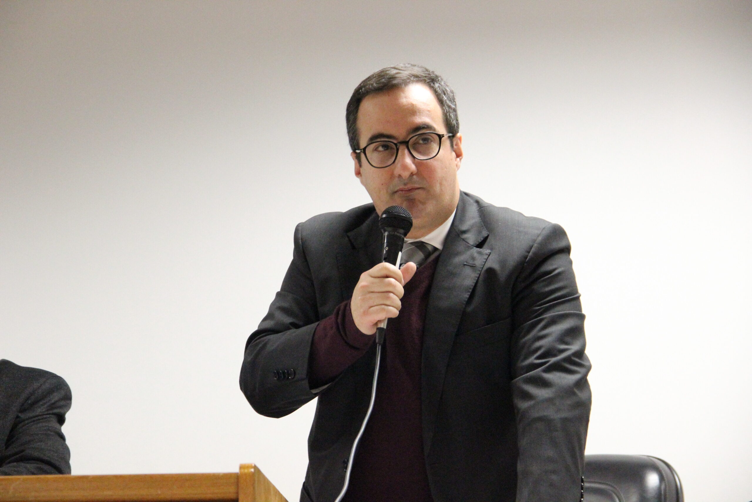 a foto mostra o juiz picarelli falando ao microfone. é um homem branca, cabelos pretos, usa óculos e veste terno