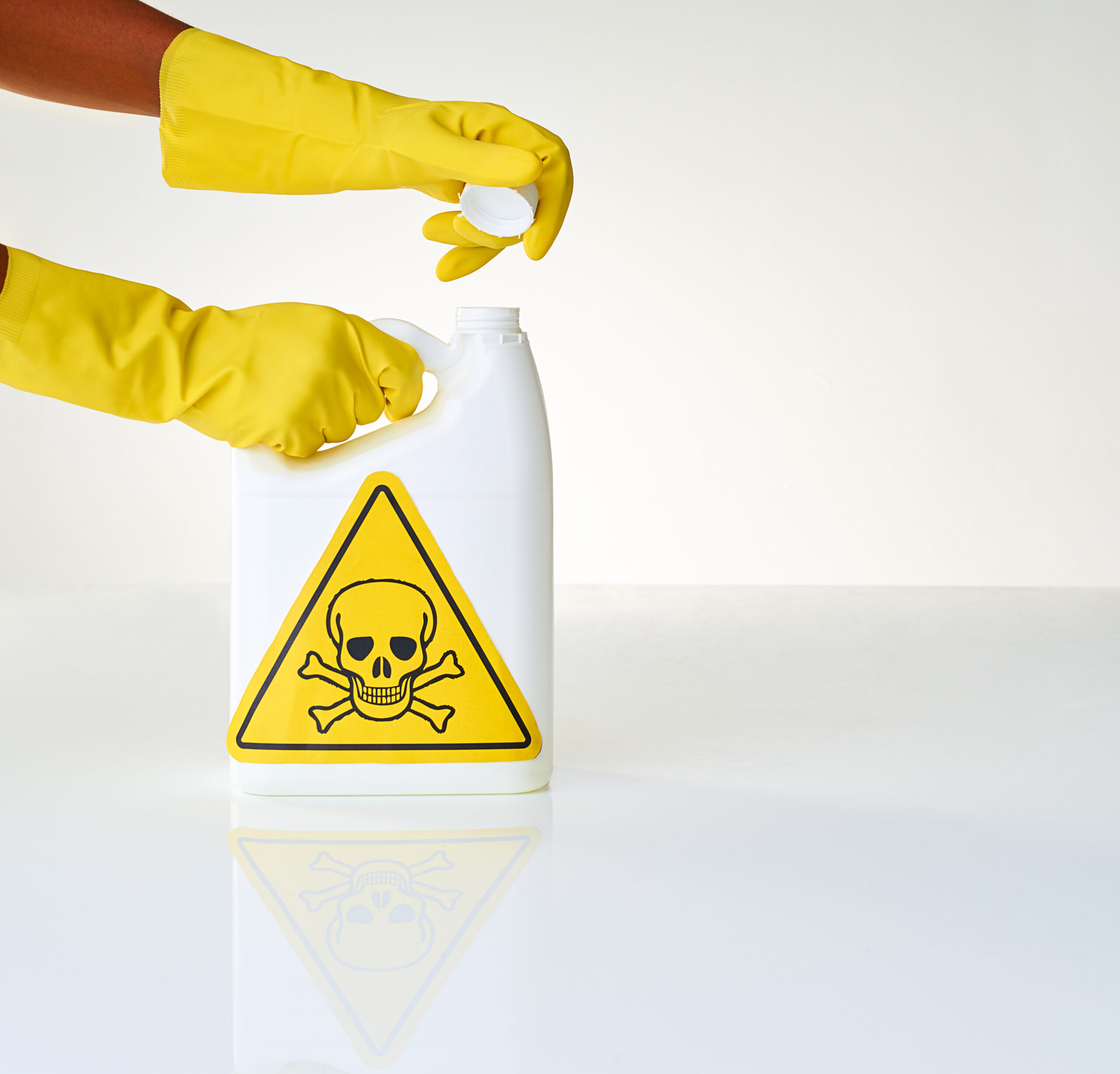a foto mostra duas mãos usando luvas de borracha. elas estão abrindo um frasco branco que tem um triângulo amarelo com uma caveira