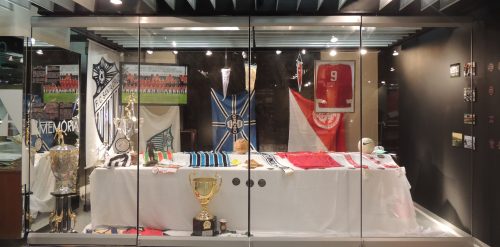 Vitrine com peças cedidas por times de futebol do Estado como camisas, bandeiras, flâmulas e faixas autografadas que contam a história de importantes conquistas da dupla Gre-nal como os campeonatos mundiais e as Libertadores da América.