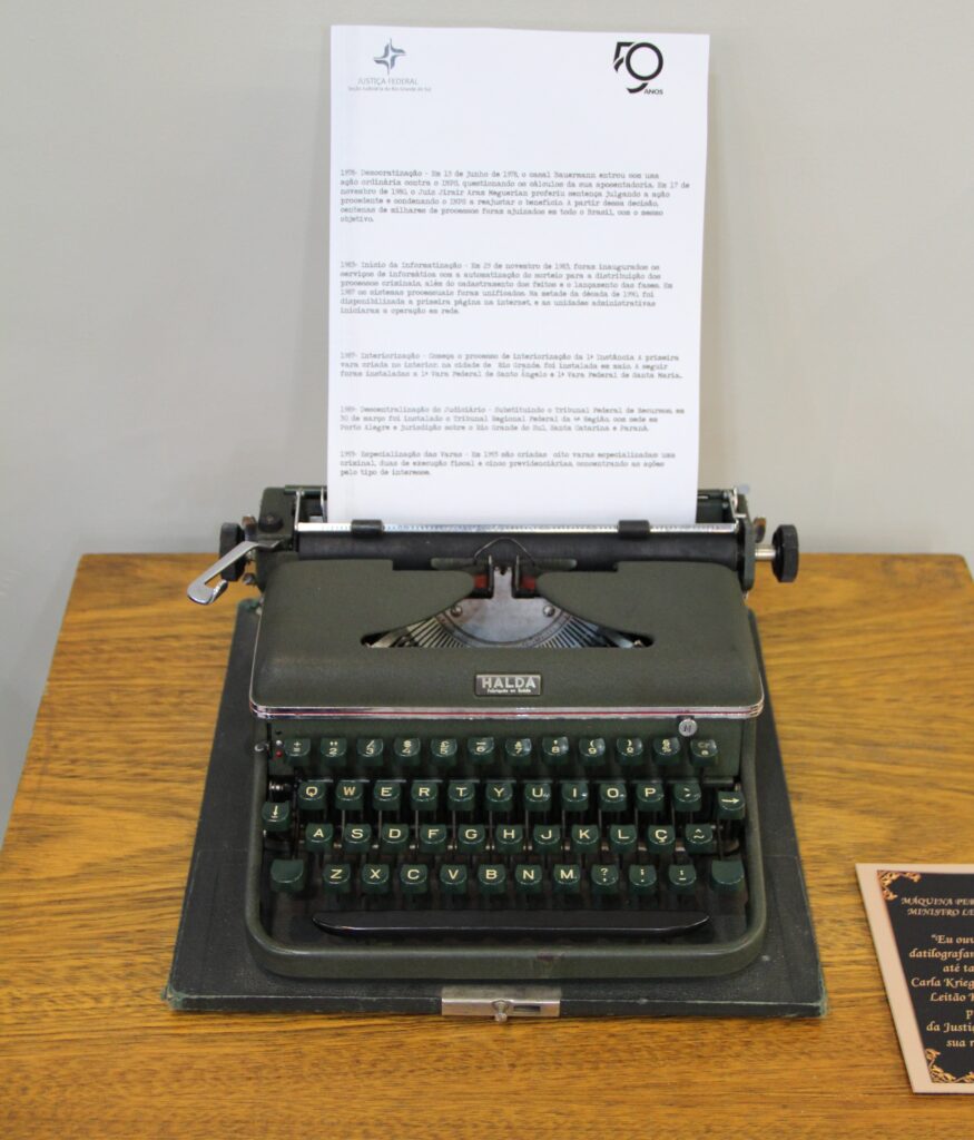 Máquina de escrever de Ministro Leitão Krieger, cor escura, em cima de uma mesa de madeira com um afolha datilografada sobre os 50 anos .
