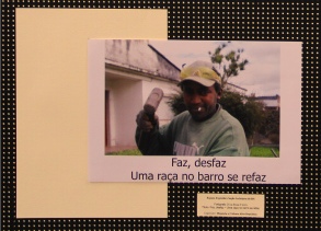 Título: “Faz, desfaz. Uma raça no barro se refaz.” Foto de um homem (do tronco para cima) também afrodescendente em local aberto, no pátio de uma casa, com um martelo de madeiro em sua mão, numa posição como se fosse martelar algo. Usa boné, um blusão verde musgo, e um cigarro na boca