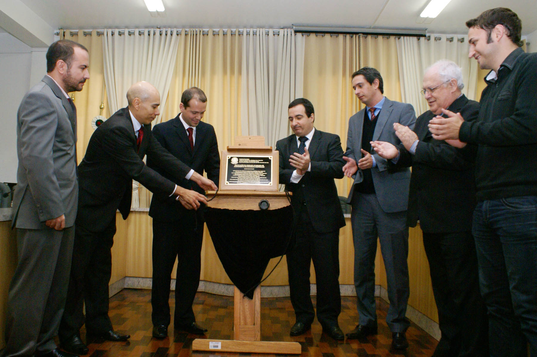 a foto mostra o descerramenta da placa de inauguração com a presença de sete homens, posicionados ao redor da placa, vestem terno.
