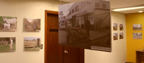 Fotos da exposição nas paredes e uma pendurada em foan. Retratam ruas e lugares por onde passam os oficiais de justiça.