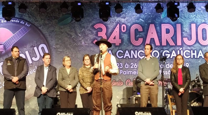 IMAGEM3 a foto mostra o palco do evento com um homem pilchado falando ao microfone. ao lado dele estão algumas pessoas, entre elas, a juíza.